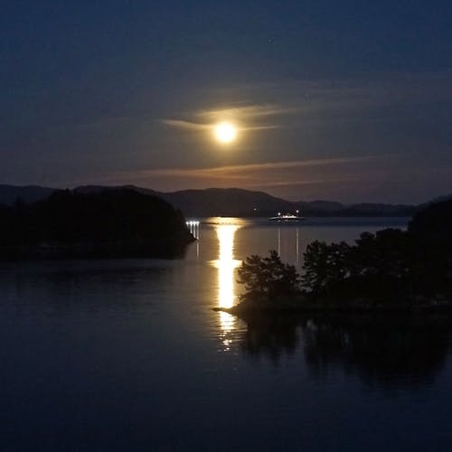 Fritidsbustad, fiskeoppdrettsanlegg og ferje spegla seg saman med månen. (Foto: Kjetil Vasby Bruarøy)